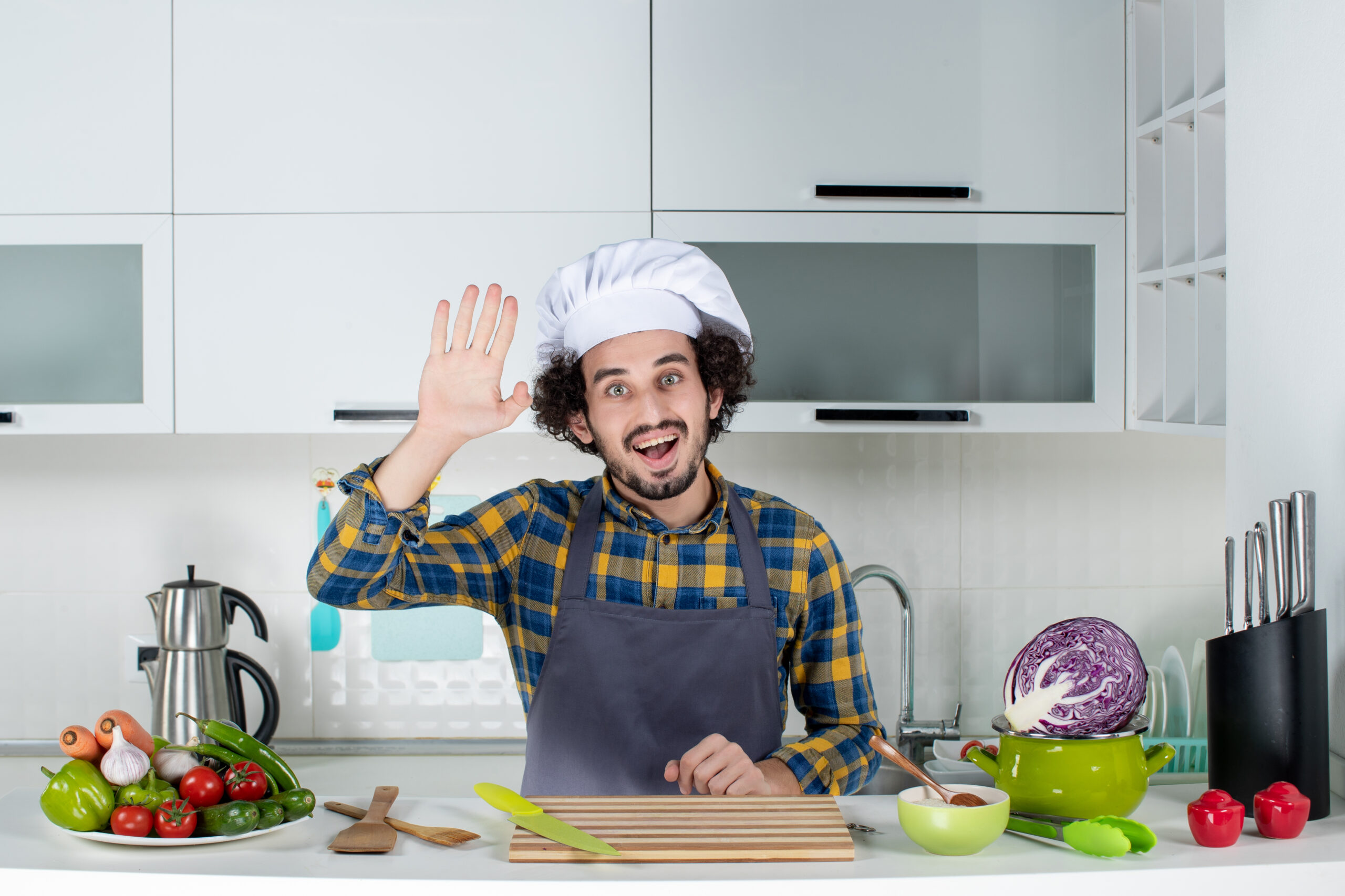 front view smiling male chef with fresh vegetables cooking with kitchen tools saying hello white kitchen scaled